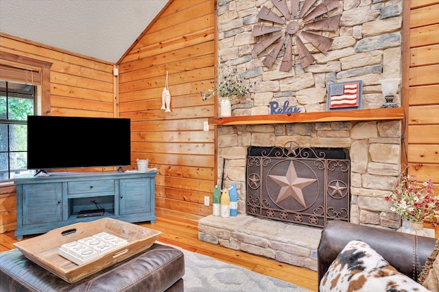 unfurnished living room with hardwood / wood-style flooring, wooden walls, vaulted ceiling, a textured ceiling, and a fireplace