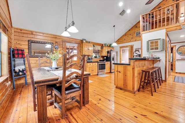 dining space featuring high vaulted ceiling, light hardwood / wood-style flooring, and wood walls