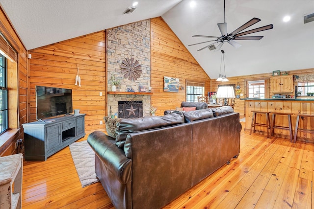 living room featuring ceiling fan, light hardwood / wood-style flooring, a stone fireplace, and wood walls