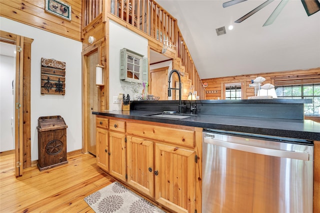 kitchen featuring lofted ceiling, light hardwood / wood-style flooring, sink, stainless steel dishwasher, and wood walls