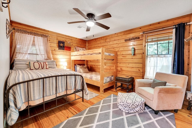 bedroom featuring ceiling fan, wood walls, wood-type flooring, and a textured ceiling