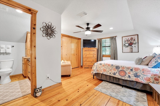 bedroom featuring lofted ceiling, light wood-type flooring, ensuite bathroom, a textured ceiling, and ceiling fan