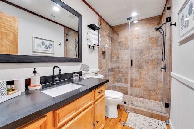 bathroom with hardwood / wood-style flooring, toilet, a shower with shower door, vanity, and crown molding