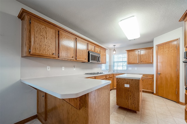 kitchen featuring sink, a textured ceiling, kitchen peninsula, hanging light fixtures, and stainless steel appliances