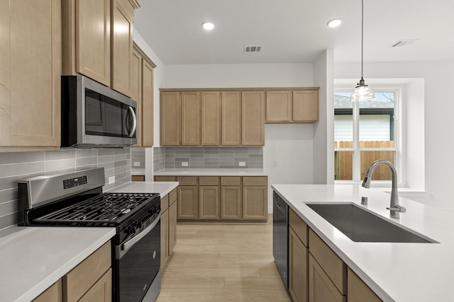 kitchen with sink, backsplash, light hardwood / wood-style floors, pendant lighting, and appliances with stainless steel finishes