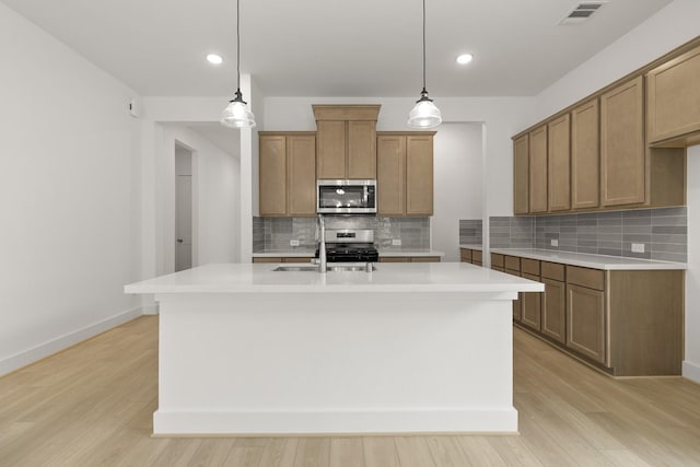 kitchen featuring a kitchen island with sink, light hardwood / wood-style flooring, stainless steel appliances, and decorative light fixtures