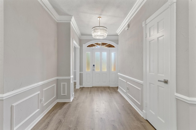 doorway to outside with light hardwood / wood-style flooring, ornamental molding, and a notable chandelier