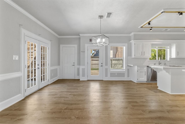 unfurnished dining area with sink, french doors, an inviting chandelier, crown molding, and wood-type flooring