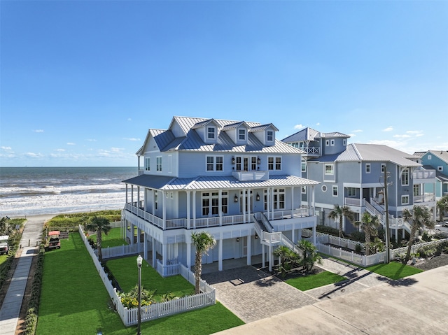 view of front facade with a water view, a view of the beach, a balcony, and a front lawn