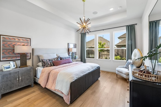 bedroom with light hardwood / wood-style floors, a notable chandelier, and a tray ceiling