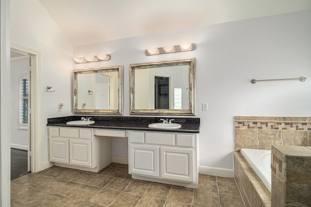 bathroom with tile patterned flooring, lofted ceiling, a relaxing tiled tub, and vanity