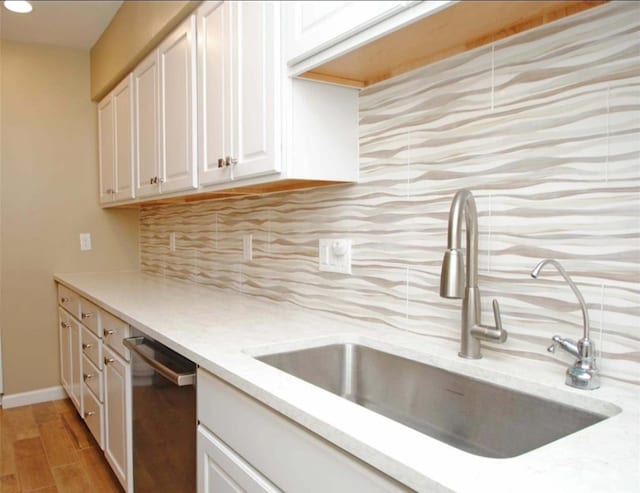 kitchen featuring backsplash, white cabinetry, stainless steel dishwasher, light hardwood / wood-style floors, and sink