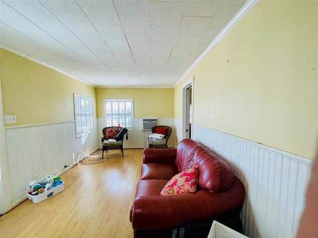 living area featuring a wainscoted wall, ornamental molding, an AC wall unit, and wood finished floors