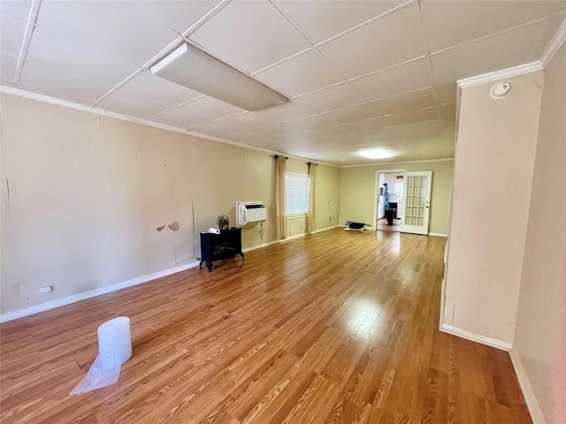 unfurnished living room with light wood-type flooring, ornamental molding, baseboards, and an AC wall unit