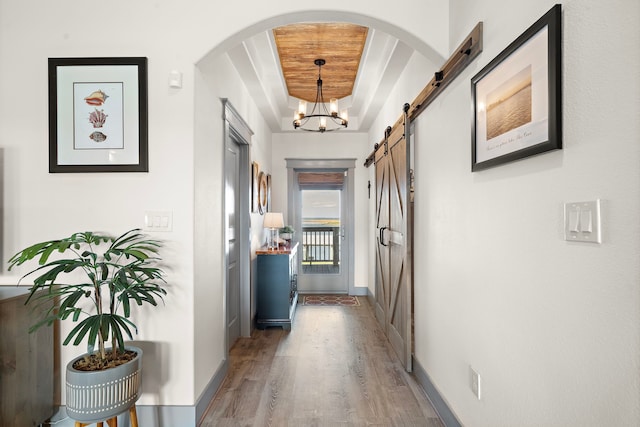 hallway featuring wood ceiling, a barn door, hardwood / wood-style flooring, and a chandelier