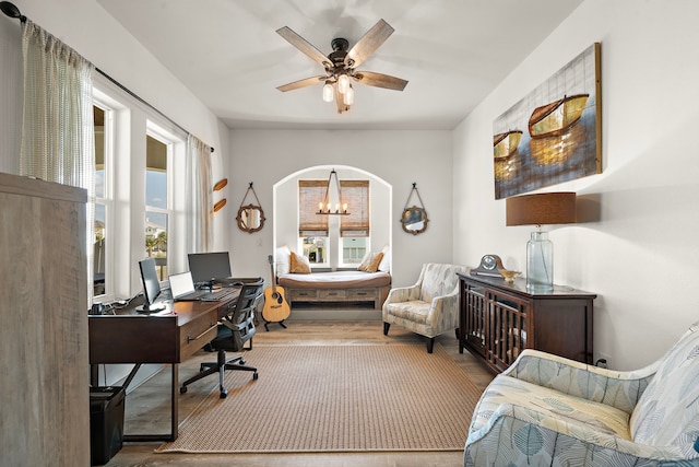 home office with ceiling fan with notable chandelier and light wood-type flooring