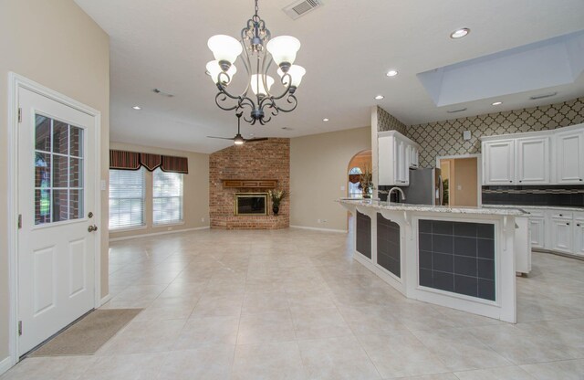 kitchen with stainless steel fridge, an island with sink, white cabinetry, a fireplace, and pendant lighting