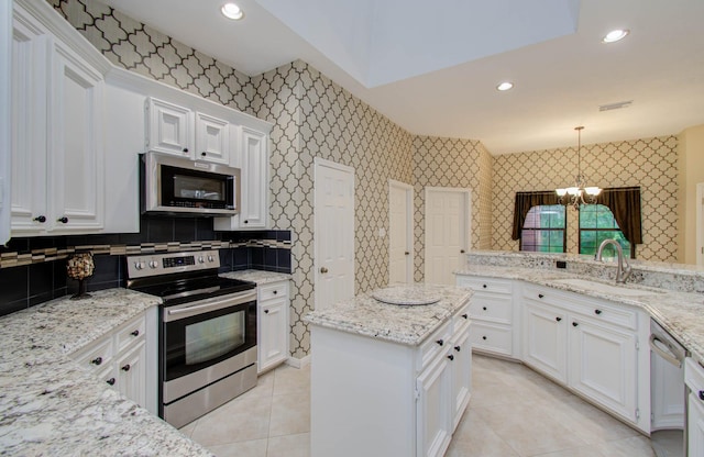 kitchen with wallpapered walls, appliances with stainless steel finishes, light stone counters, decorative light fixtures, and a sink