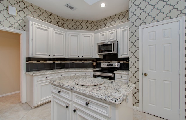 kitchen featuring light stone countertops, light tile patterned flooring, appliances with stainless steel finishes, a center island, and white cabinets