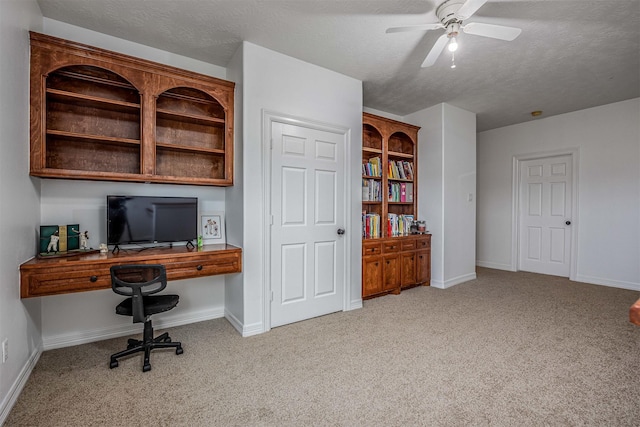 office space featuring ceiling fan, light colored carpet, built in desk, and a textured ceiling