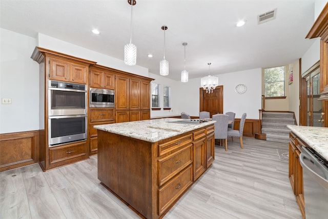 kitchen featuring a kitchen island, pendant lighting, an inviting chandelier, light wood-type flooring, and appliances with stainless steel finishes