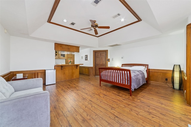 bedroom featuring wood walls, a raised ceiling, ceiling fan, hardwood / wood-style flooring, and ornamental molding