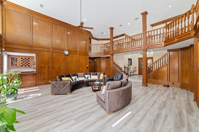 living room with a towering ceiling, crown molding, light wood-type flooring, and ceiling fan