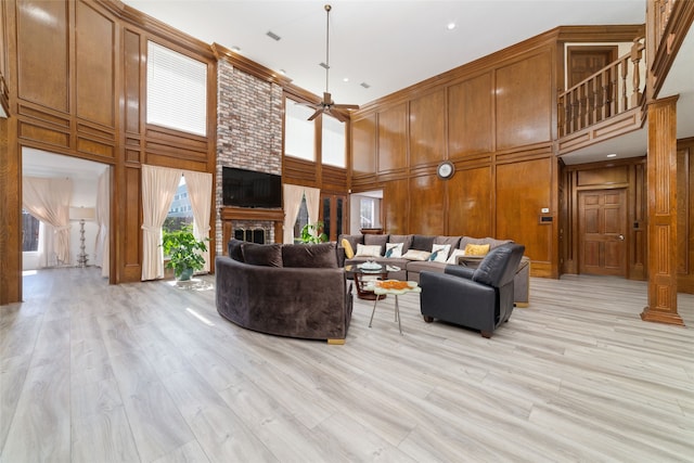 living room featuring a towering ceiling, a fireplace, light hardwood / wood-style floors, ceiling fan, and wooden walls