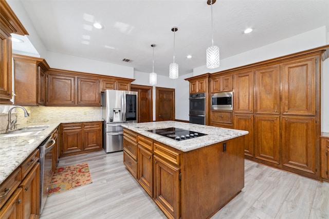 kitchen featuring appliances with stainless steel finishes, sink, a kitchen island, hanging light fixtures, and light hardwood / wood-style floors