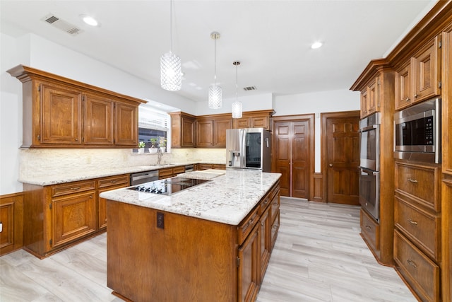 kitchen with stainless steel appliances, sink, a center island, decorative light fixtures, and light wood-type flooring