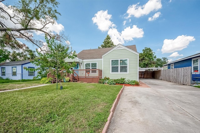 view of front of property with concrete driveway, a front lawn, fence, a wooden deck, and roof with shingles