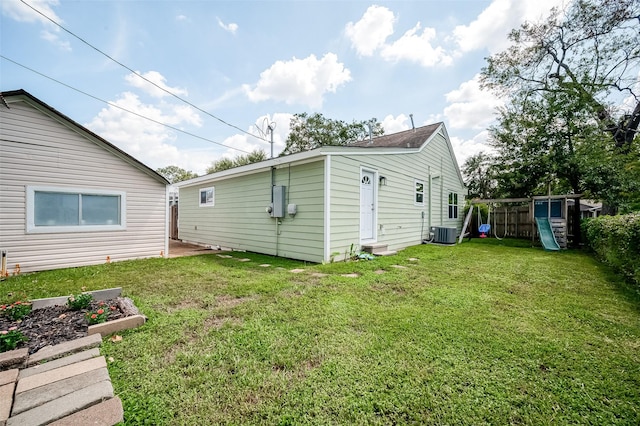 rear view of house with central air condition unit, a lawn, a garden, and a playground