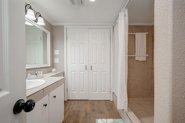 bathroom featuring a tile shower, wood finished floors, visible vents, vanity, and crown molding