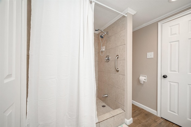 bathroom featuring a tile shower, baseboards, crown molding, and wood finished floors