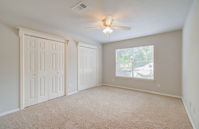 unfurnished bedroom featuring ceiling fan, carpet flooring, and two closets