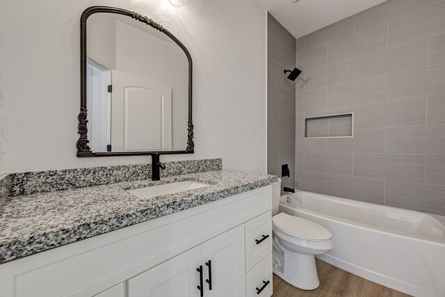 full bathroom with toilet, tiled shower / bath, hardwood / wood-style flooring, and vanity