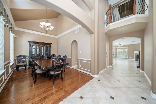 dining room with ceiling fan with notable chandelier, light wood-type flooring, ornamental molding, and a high ceiling