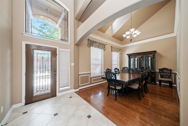 dining room with a healthy amount of sunlight, light wood-type flooring, a towering ceiling, and an inviting chandelier