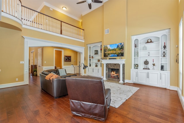 living room featuring a premium fireplace, a towering ceiling, dark hardwood / wood-style flooring, and ornamental molding