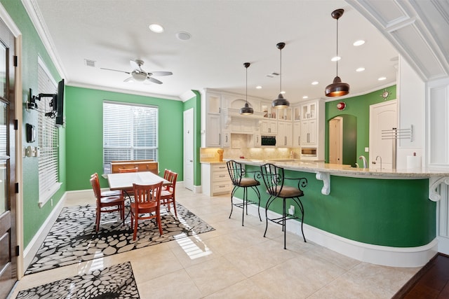 kitchen with hanging light fixtures, ceiling fan, a kitchen bar, crown molding, and light stone counters