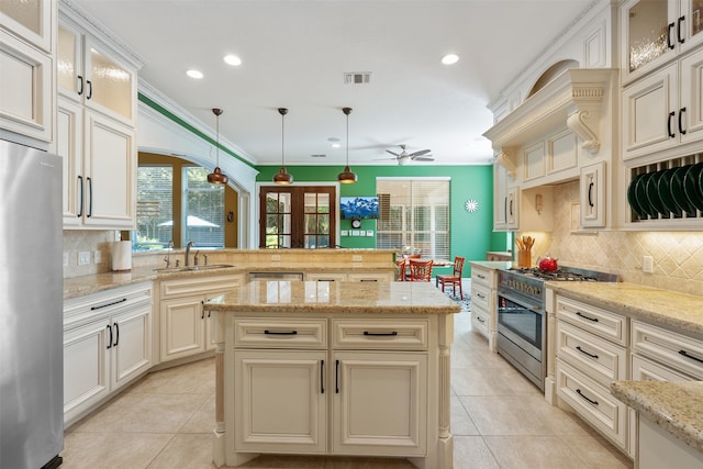 kitchen featuring ceiling fan, light stone countertops, pendant lighting, cream cabinetry, and stainless steel appliances