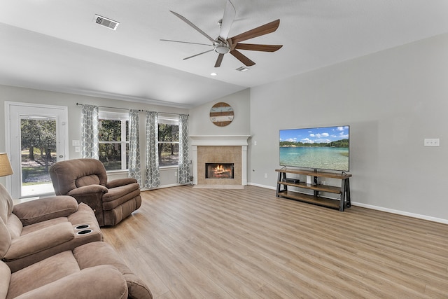 living room with lofted ceiling, a tiled fireplace, light wood-type flooring, and ceiling fan