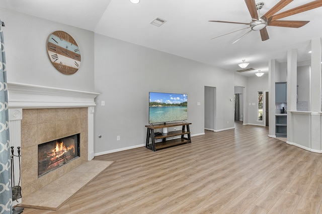 living room featuring a tiled fireplace, light hardwood / wood-style flooring, and ceiling fan