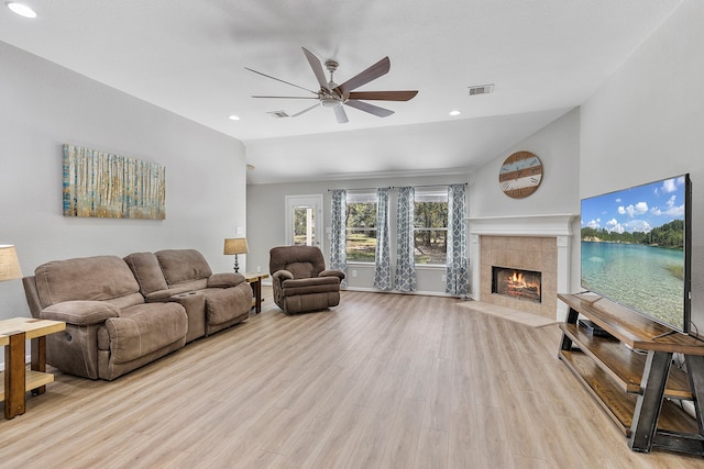 living room with lofted ceiling, a tiled fireplace, light wood-type flooring, and ceiling fan