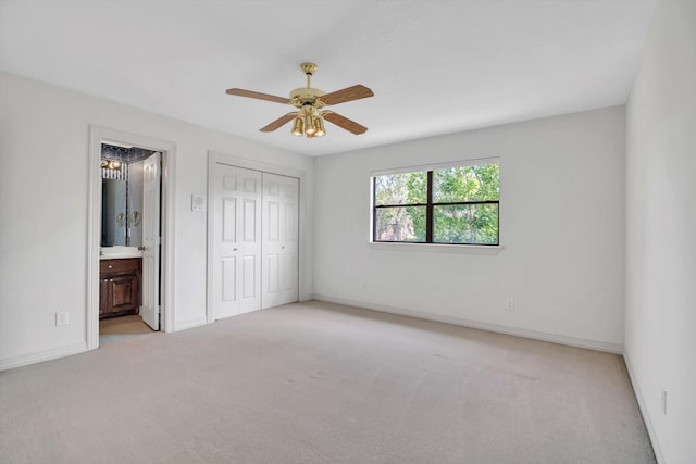 unfurnished bedroom featuring light carpet, a closet, ensuite bathroom, and ceiling fan