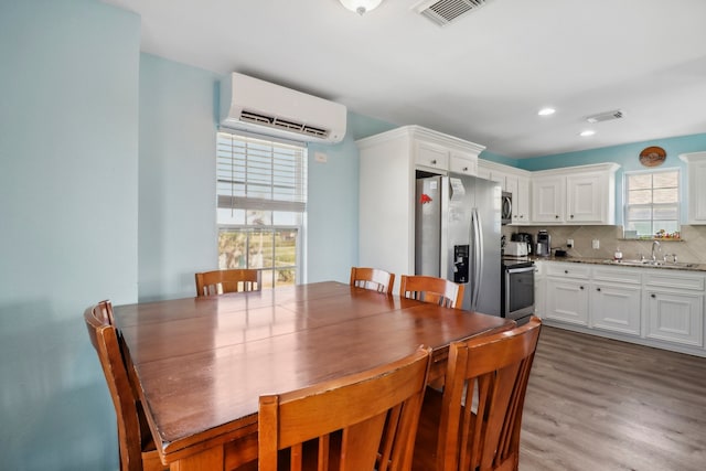 dining room with a wall mounted air conditioner, sink, wood-type flooring, and plenty of natural light