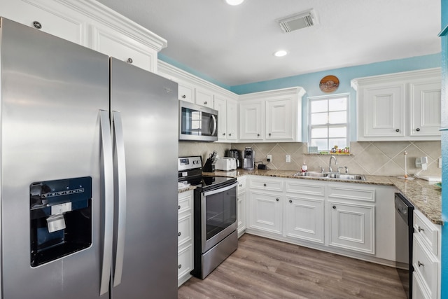 kitchen featuring light stone countertops, appliances with stainless steel finishes, sink, white cabinetry, and hardwood / wood-style flooring