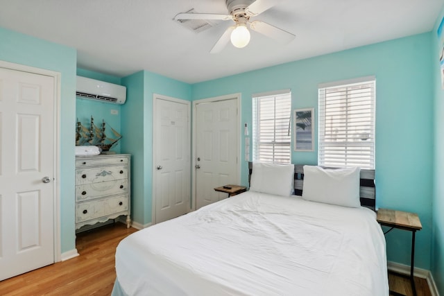 bedroom featuring a wall mounted air conditioner, light hardwood / wood-style floors, and ceiling fan