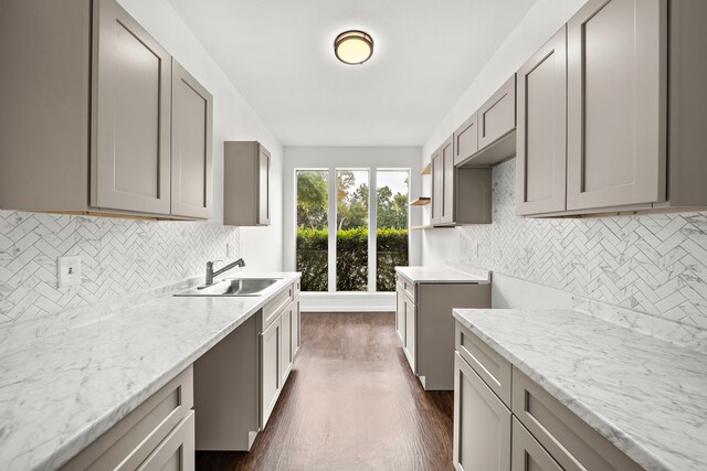 kitchen featuring sink, gray cabinetry, dark hardwood / wood-style floors, light stone counters, and tasteful backsplash