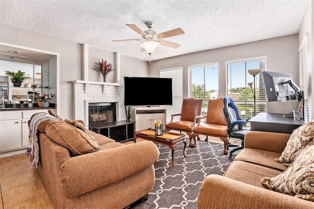 tiled living room featuring a textured ceiling, ceiling fan, and a brick fireplace